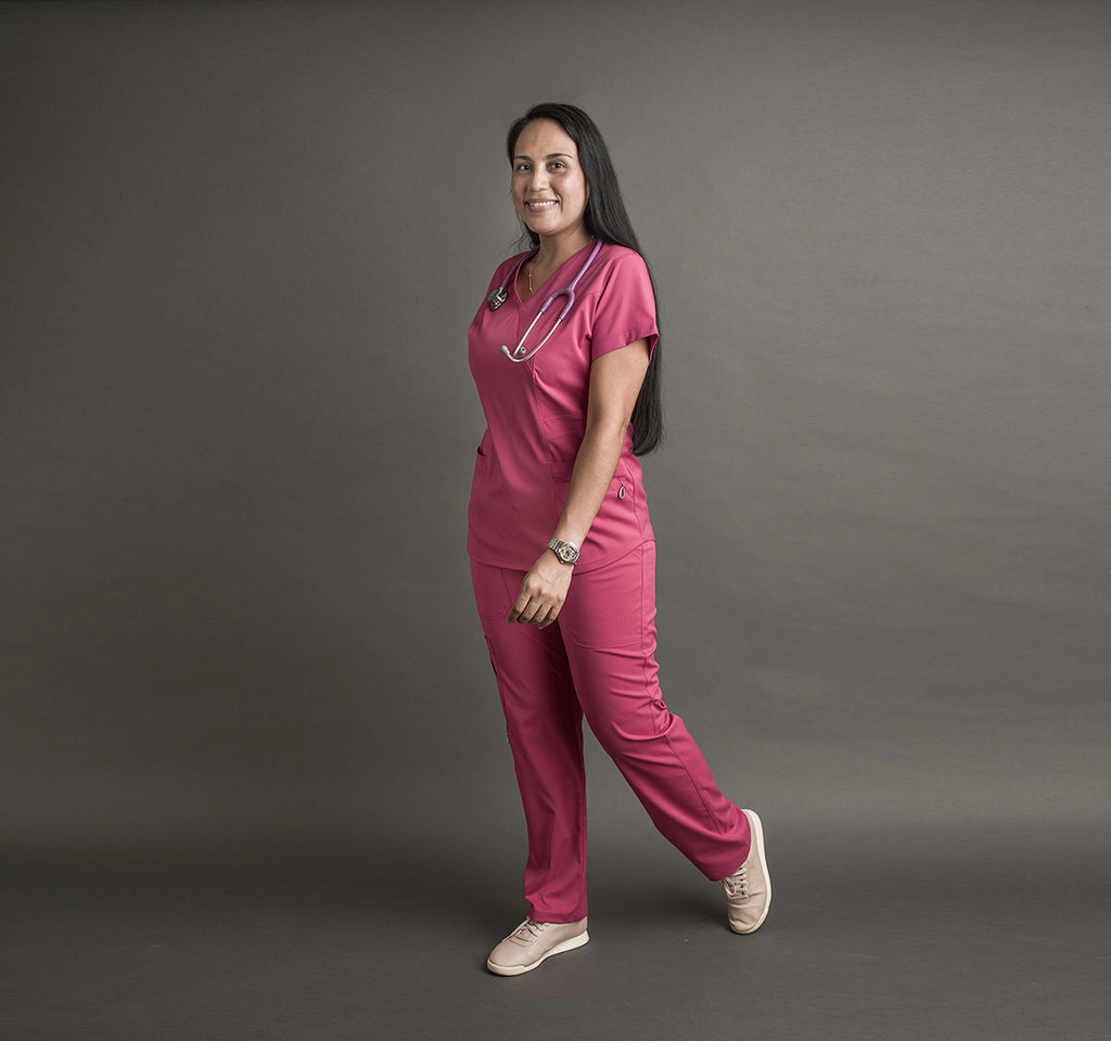 Una mujer usa unos scrubs color rosa. Lleva un estetoscopio alrededor del cuello.