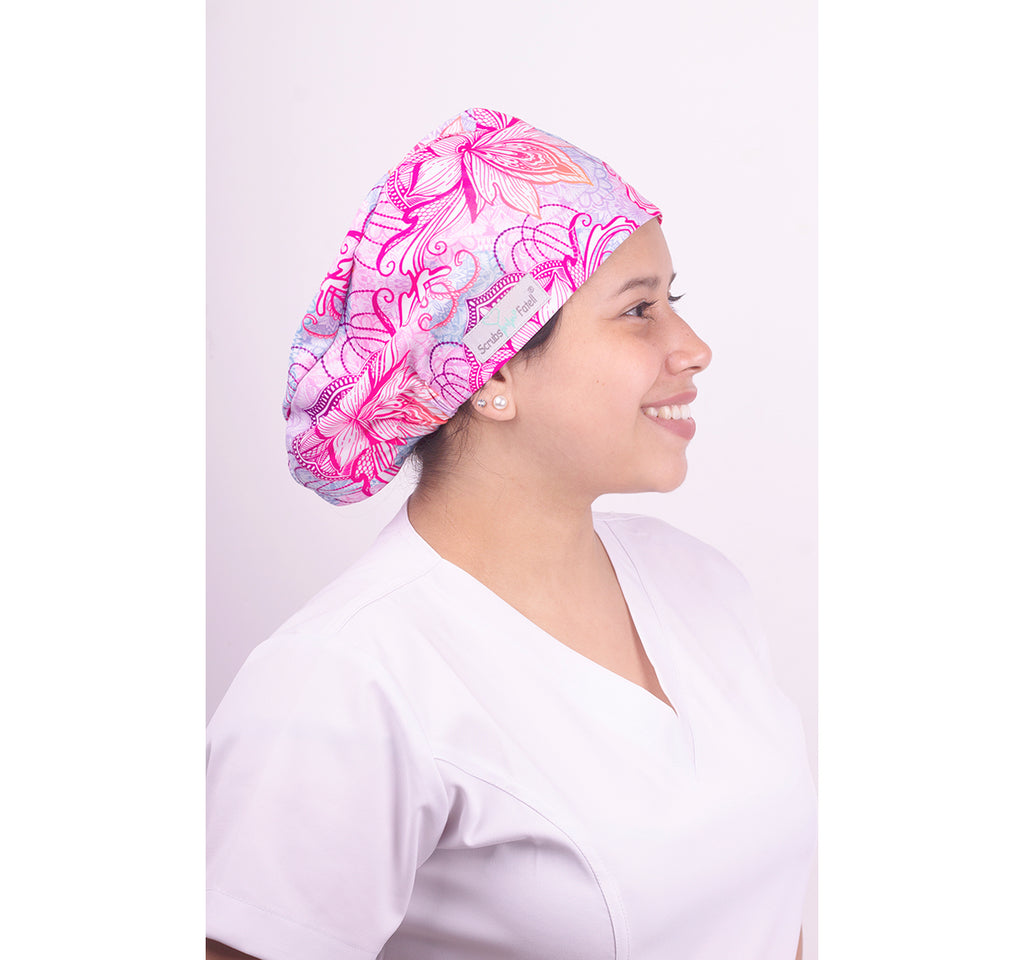 Mujer usando un gorro quirúrgico con una horma elástica. Tiene un estampado de flores rosadas.