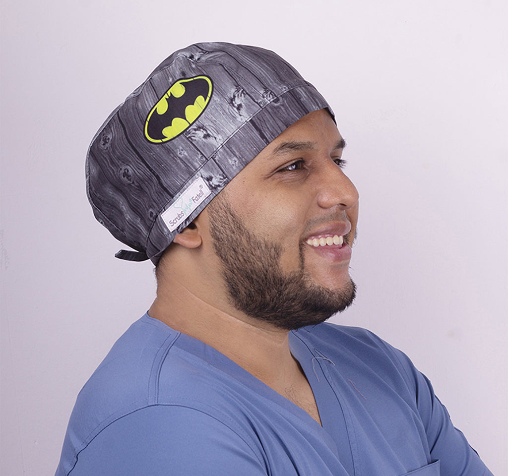Un hombre usando un gorro quirúrgico con amarre. Tiene un estampado de el ícono de Batman sobre un fondo gris..