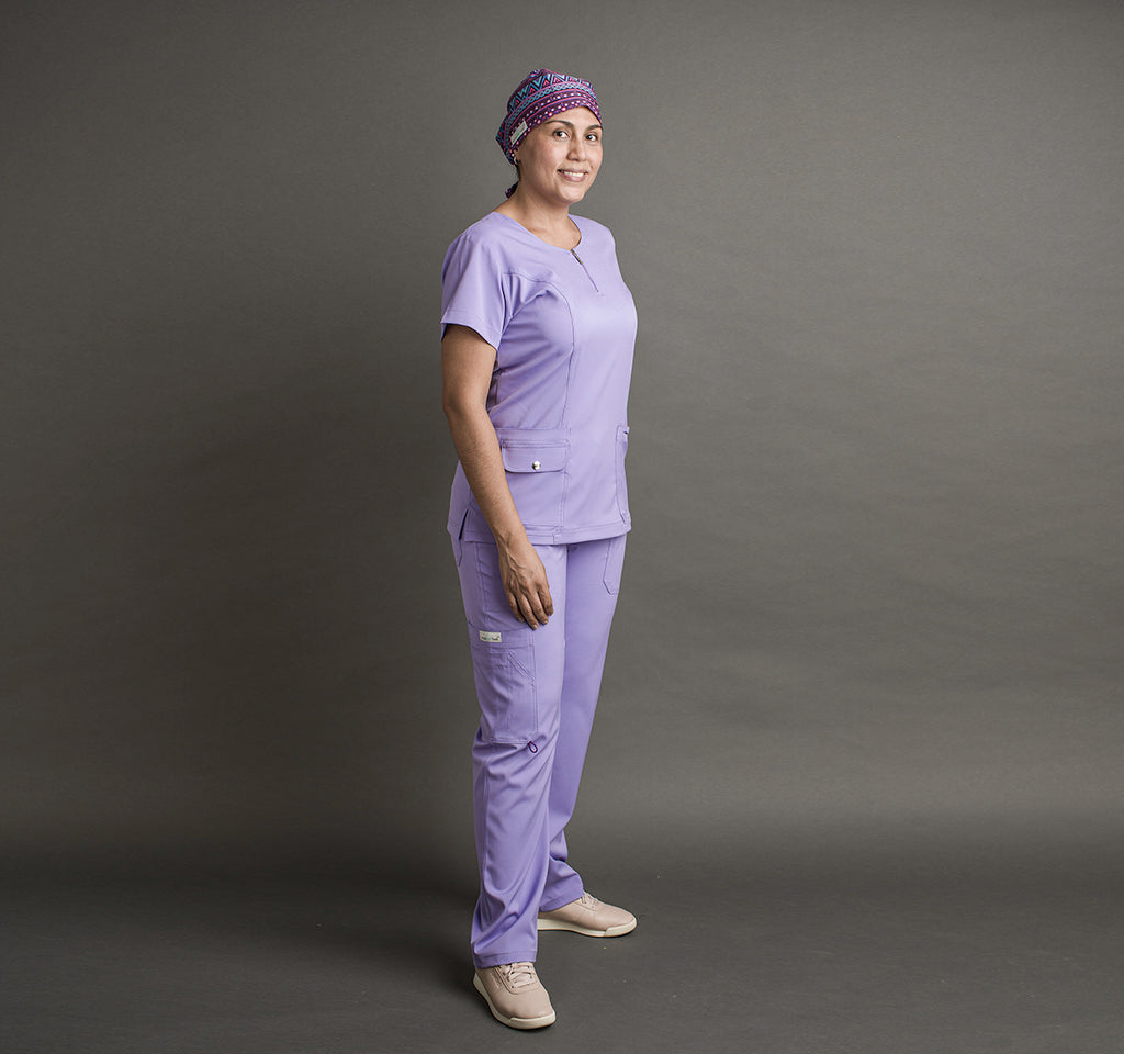 Una mujer usa unos scrubs color lila. Lleva un gorro quirúrgico en la cabeza.