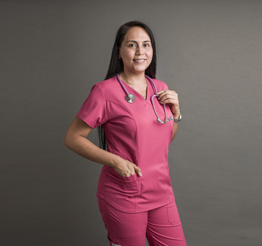 Una mujer usa unos scrubs color rosa. Lleva un estetoscopio alrededor del cuello.