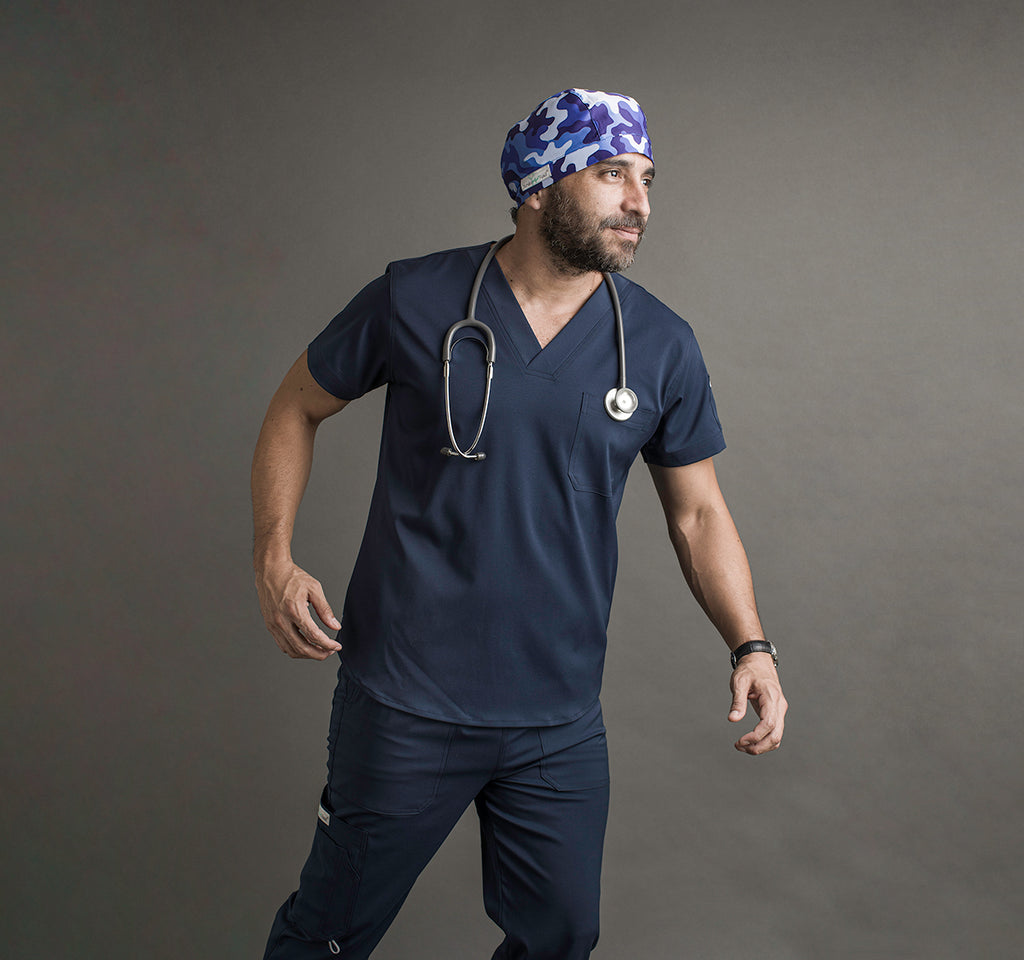 Un hombre usando un scrub color azul oscuro. Lleva un estetoscopio alrededor del cuello y un gorro quirúrgico en la cabeza.