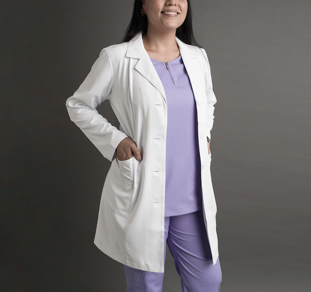 Una mujer usa un mandil blanco sobre unos scrubs color lila.
