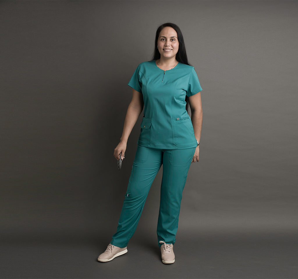 Una mujer usa unos scrubs color verde agua. Lleva un estetoscopio en la mano.