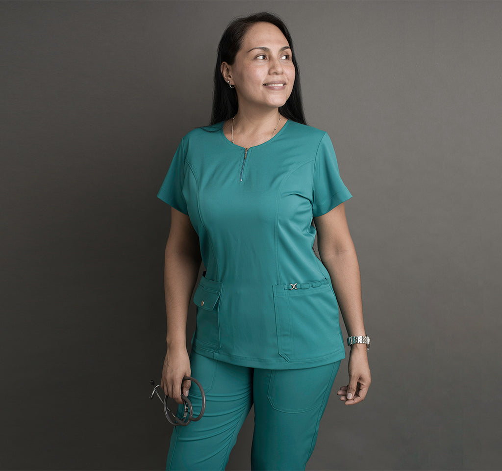 Una mujer usa unos scrubs color verde agua. Lleva un estetoscopio en la mano.